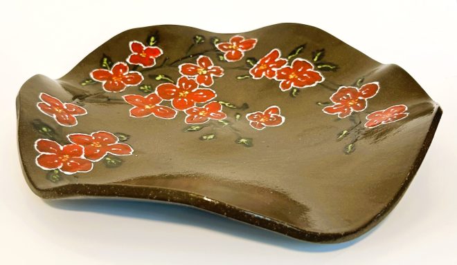 Dark brown clay base. Wavy surface. Hand painted flower detail. Clear glaze cover. Diameter-11in.