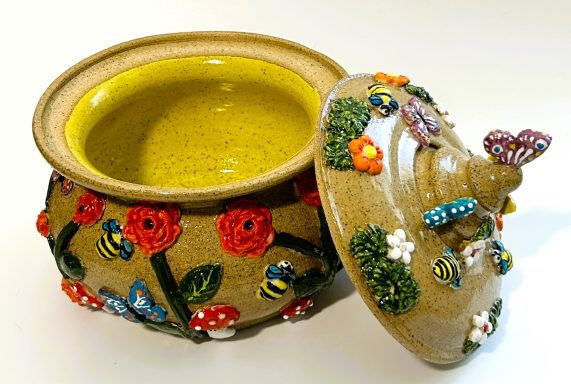 Speckled clay body. Whimsical lidded pot with garden themed hand painted appliques. Yellow glazed interior. H-7in x Diameter-6.5in.