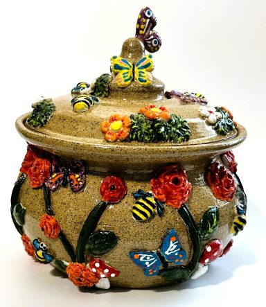 Speckled clay body. Whimsical lidded pot with garden themed hand painted appliques. Yellow glazed interior. H-7in x Diameter-6.5in.